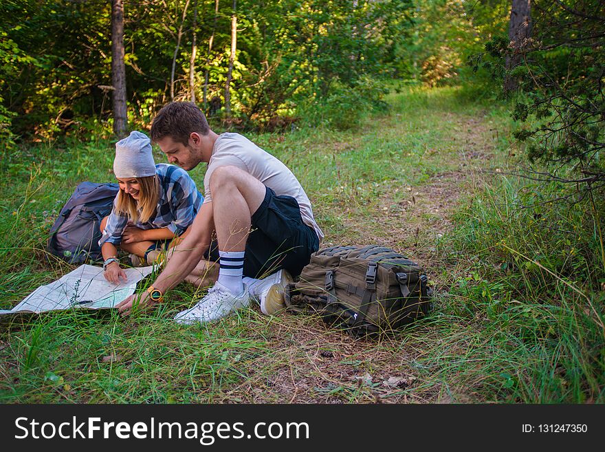Young couple examining the map inside the forest. Hiking concept