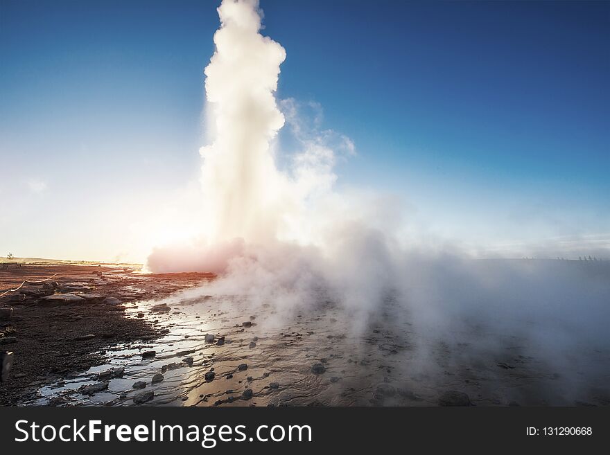 Strokkur geyser eruption in Iceland. Fantastic colors shine through the steam. Beautiful pink clouds in a blue sky.