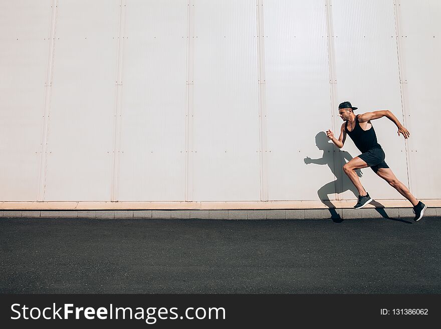Young man runner running along wall with copy space