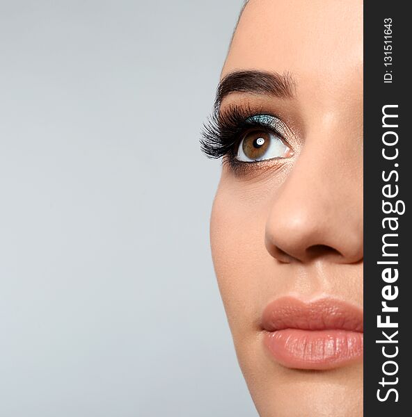 Young woman with eyelash extensions and beautiful makeup on light background.