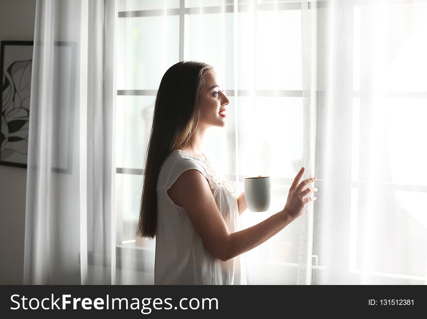 Young woman standing near window with curtains