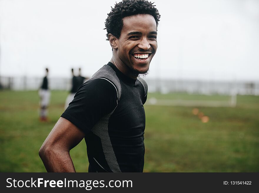 Portrait of a cheerful footballer standing on field during practice. Side view of an african soccer player standing on football
