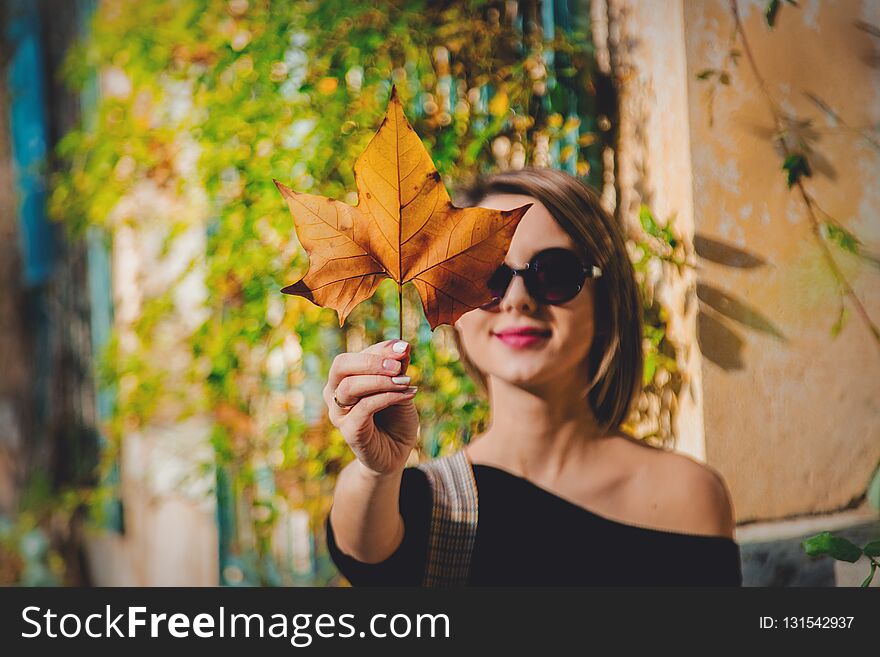Young girl in sunglasses holding a leaf in hands and looking on it. Autumn season time