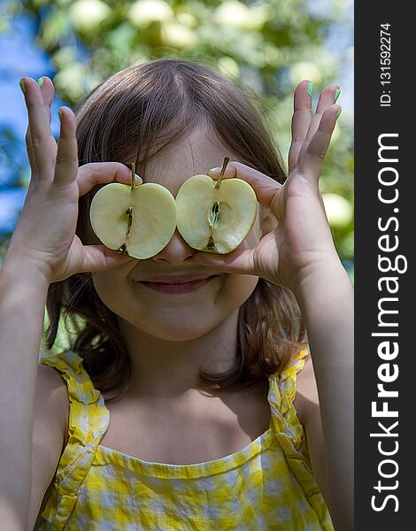 Girl at eye level holding two halves of apples. Behind her you can see the sky and Apple tree. Girl at eye level holding two halves of apples. Behind her you can see the sky and Apple tree