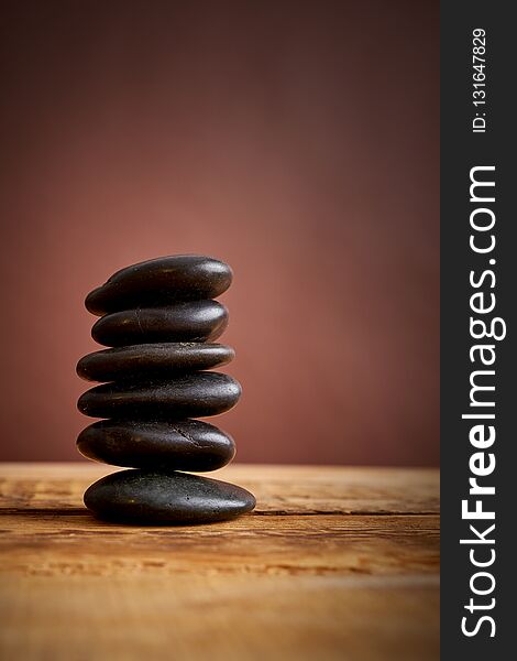 Stack of black spa stones for massage on a brown background and an wooden table