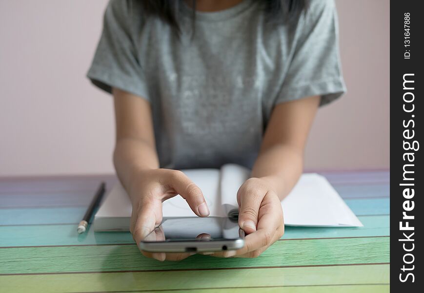 A little girl playing smartphone with doing homework on the colourful table