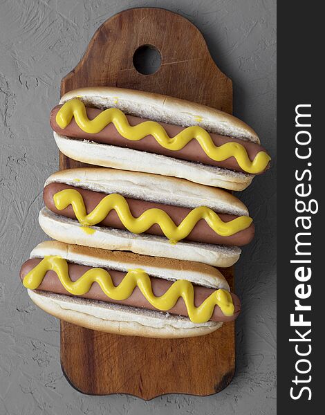 Homemade hot dogs with yellow mustard on wooden board over grey background, overhead view. Flat lay, from above. Closeup
