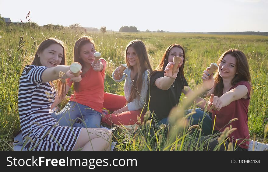 Five Young Schoolgirls Eat Ice Cream On A Meadow On A Warm Summer Day.