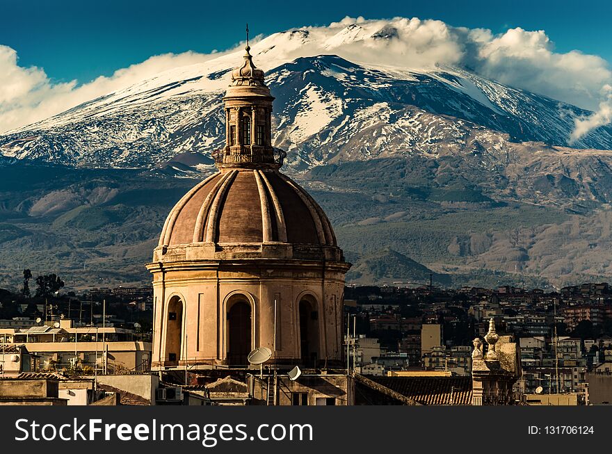 The dome of Cathedral in Catania on the background of volcano Etna in the snow. The view of the city of Catania with the view of Etna volcano, Sicily, Italy. Catania the UNESCO World Heritage.