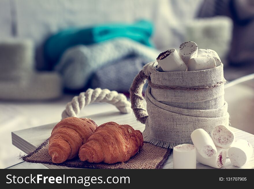 Cozy winter still life, consist of, cup of coffee, marshmallow, croissants and fur shoes with sweaters in the home interior