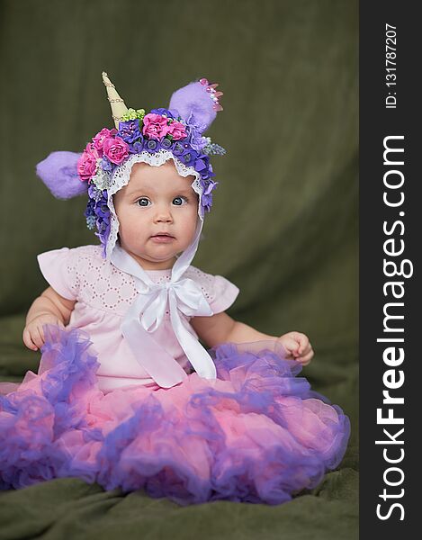 ЖAdorable Ten month old newborn baby girl sitting on green carpet. Copy space. Portrait of toddler indoor. Baby in unicorn hat