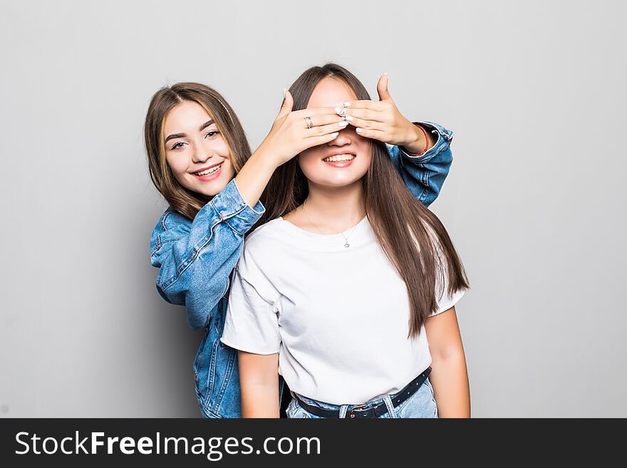 Portrait of two ladies friends looking camera covering eyes with hands standing isolated over gray background