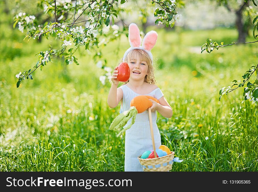 Cute funny girl with Easter eggs and bunny ears at garden. easter concept. Laughing child at Easter egg hunt. Child in park with basket full of eggs, spring concept