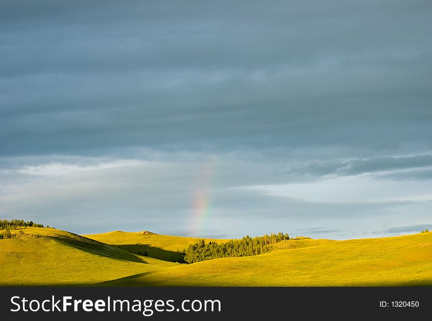 Cloudy sky with rainbow and fields