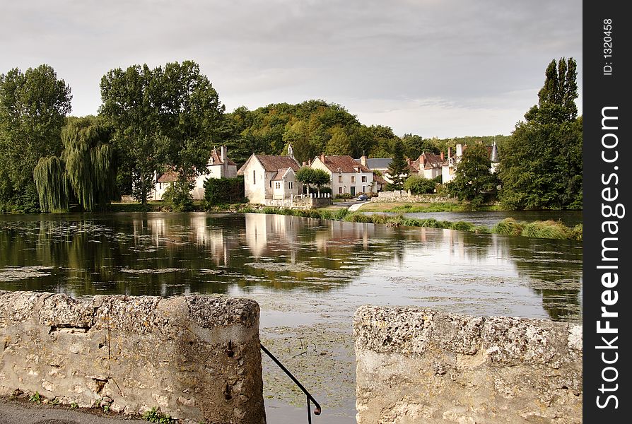 View over a tranquil river towards a rustic rural Village in France