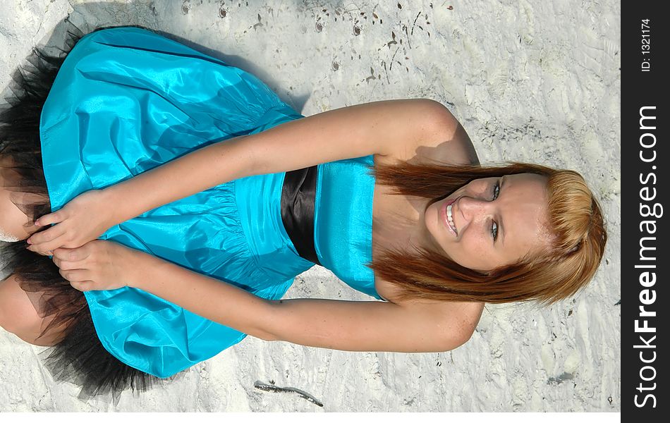 A pretty teen sitting in the sand on the beach in a formal dress. A pretty teen sitting in the sand on the beach in a formal dress.