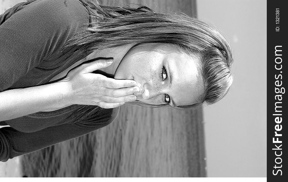 A pretty teenager with her hands over her mouth indicating silence in black and white