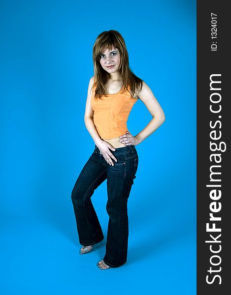 Beautiful young girl posing in a studio, holding her hands on the hips, isolated on blue background.