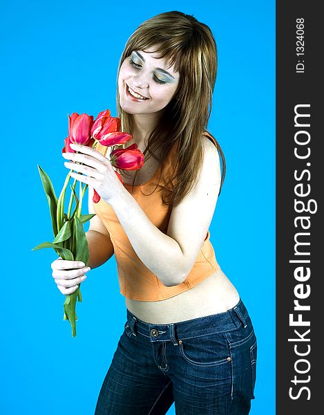 Portrait of a young girl smiling and looking at a bouquet of tulips, expression of youth and happiness; nice make-up, isolated on blue background. Portrait of a young girl smiling and looking at a bouquet of tulips, expression of youth and happiness; nice make-up, isolated on blue background.