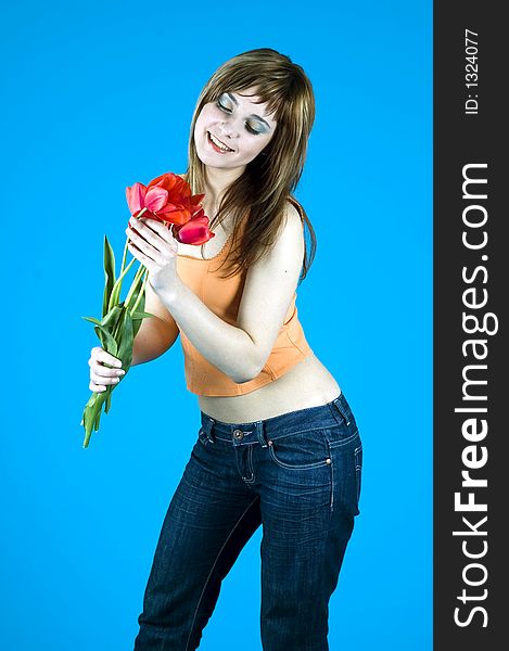 Portrait of a young girl smiling and looking at a bouquet of tulips, expression of youth and happiness; nice make-up, isolated on blue background. Portrait of a young girl smiling and looking at a bouquet of tulips, expression of youth and happiness; nice make-up, isolated on blue background