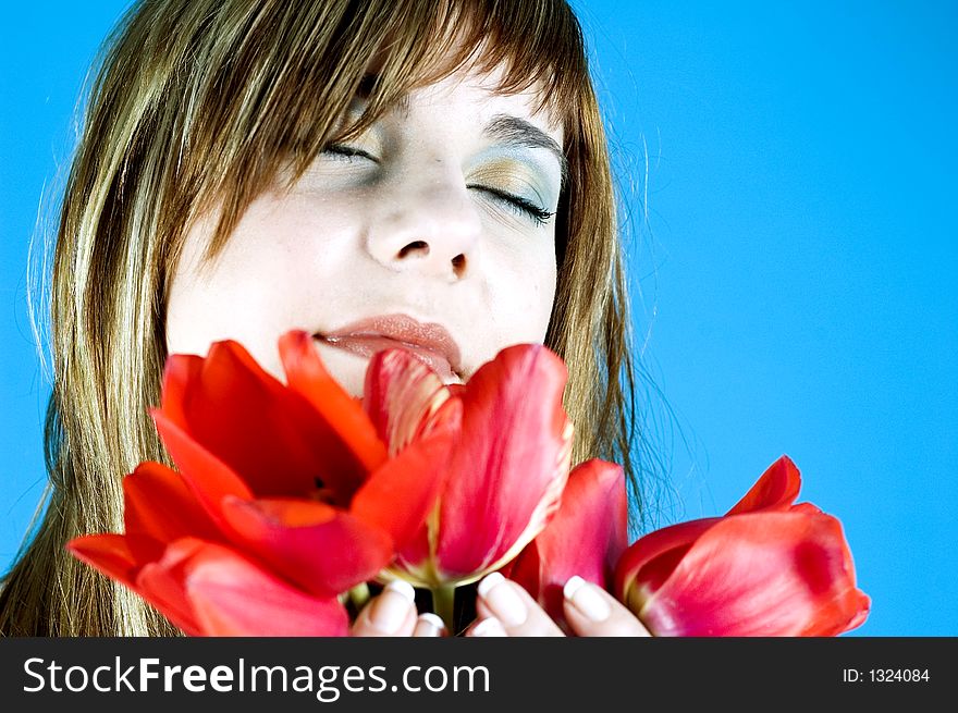 Portrait of a young beautiful girl, smelling a bouquet of tulips and looking relaxed due to the nice scent of the flowers; expression of youth and senses; isolated on blue. Portrait of a young beautiful girl, smelling a bouquet of tulips and looking relaxed due to the nice scent of the flowers; expression of youth and senses; isolated on blue.
