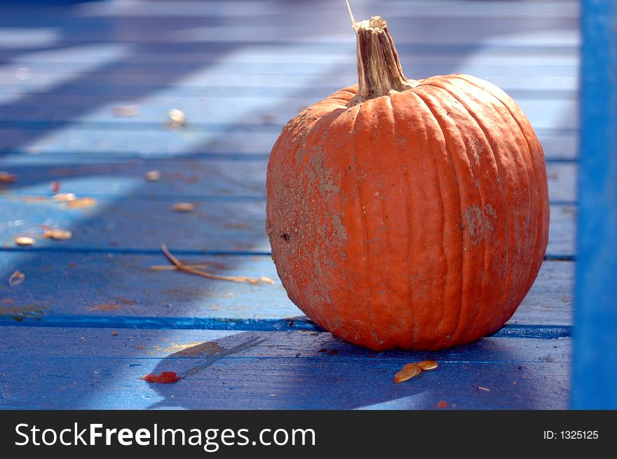 A single orange pumpkin on a blue deck with shadows from the sun. A single orange pumpkin on a blue deck with shadows from the sun.