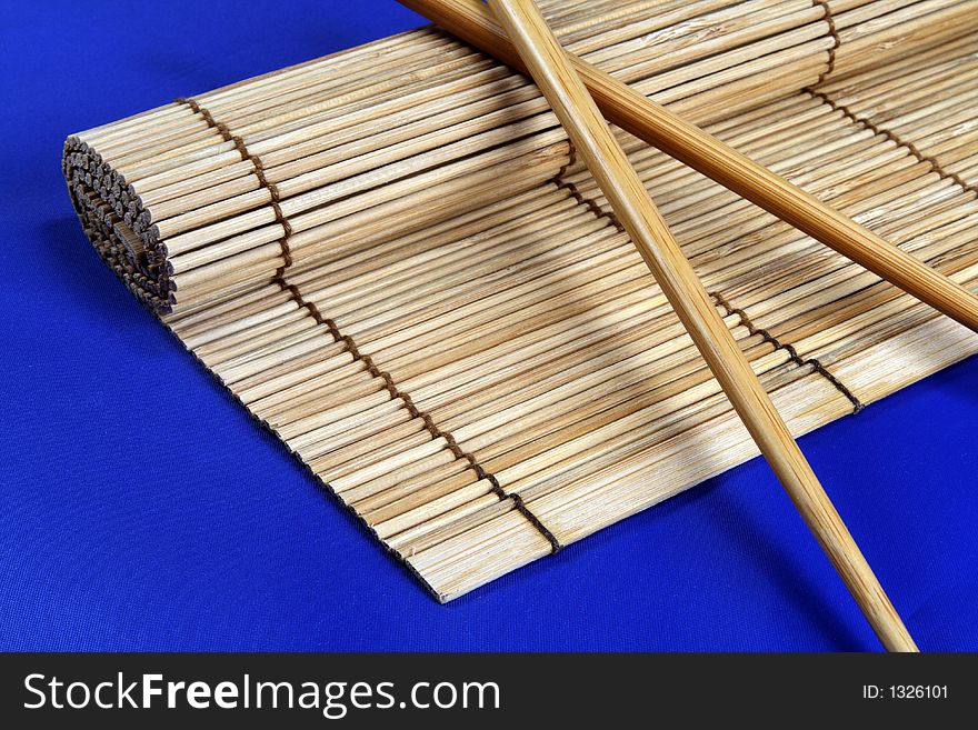 Chopsticks and bamboo mat isolated on blue