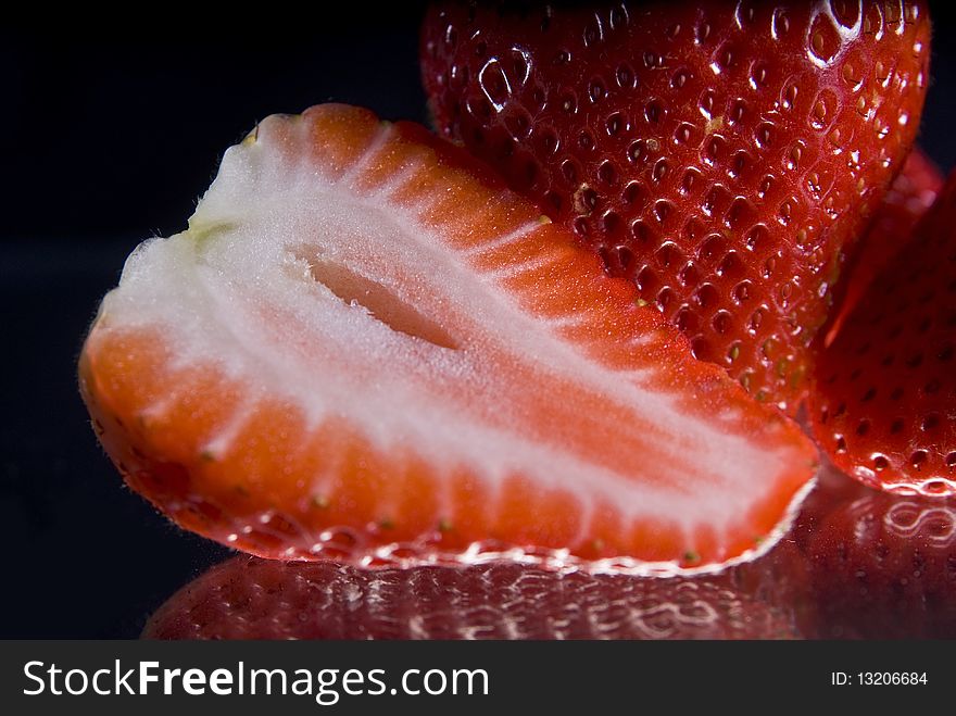 Closeup of whole and sliced strawberries reflecting on black background. Closeup of whole and sliced strawberries reflecting on black background.
