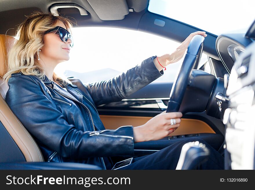 Photo of side of young blonde in black glasses sitting in car during day. Photo of side of young blonde in black glasses sitting in car during day