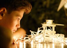 Cute Young Boy In White T Shirt Looks At Lights In The Evening At Home In Front Of Fir Tree With Lights. Stock Images