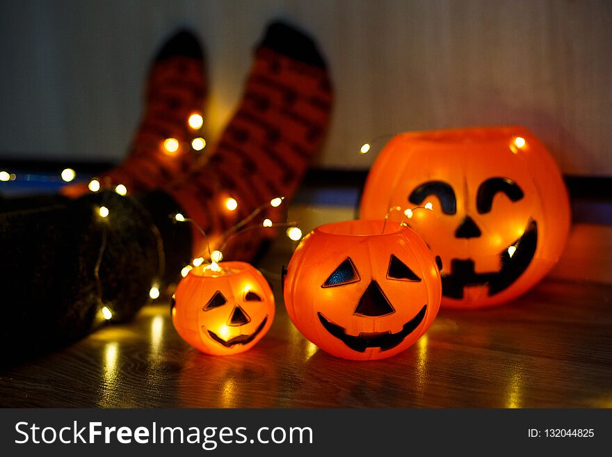 Kids legs in stylish warm bright colorful striped funny socks in garland lights on floor with pumpkins in room. decor for Halloween, cosy moment. cozy autumn days. Happy Halloween celebration concept