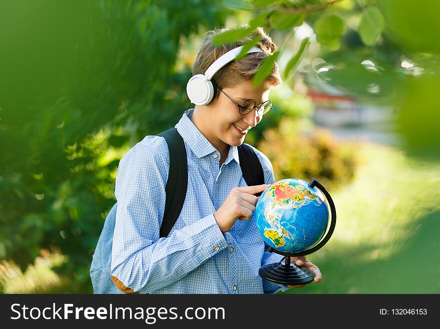 Young Boy In Blue Shirt And Round Glasses Looks And Points On Globe In His Hands. Education, Back To School