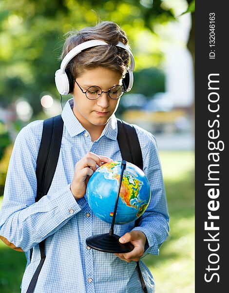 Young boy in blue shirt and round glasses looks and points on globe in his hands. Education, back to school concept