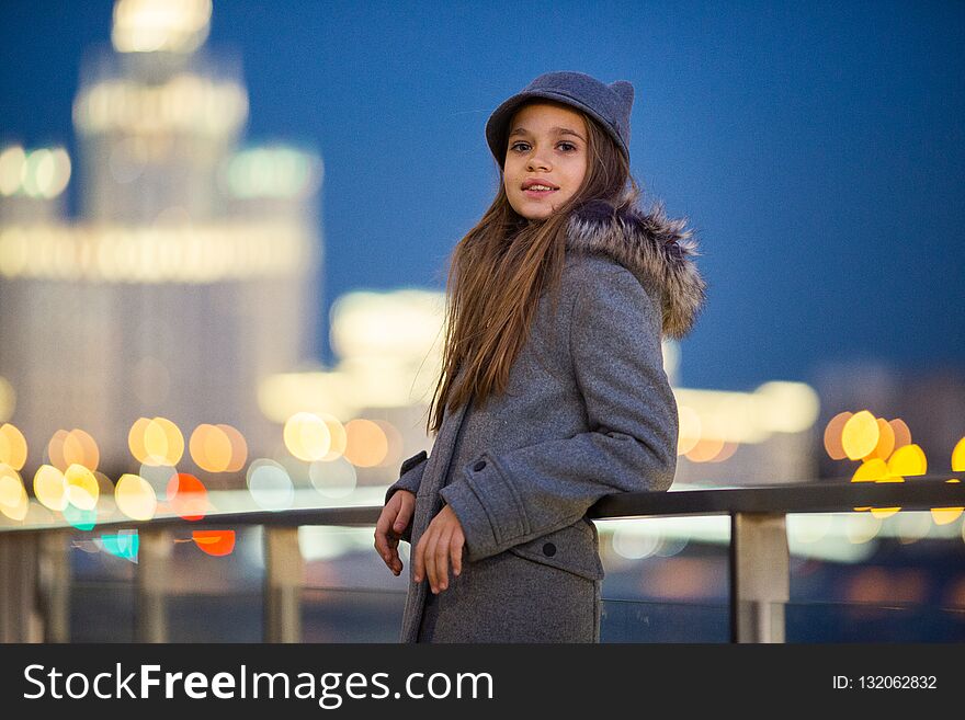 Photo Of Girl In Gray Hat And Coat On Waterfront On Background Of Spots, Lights, Blurred Background