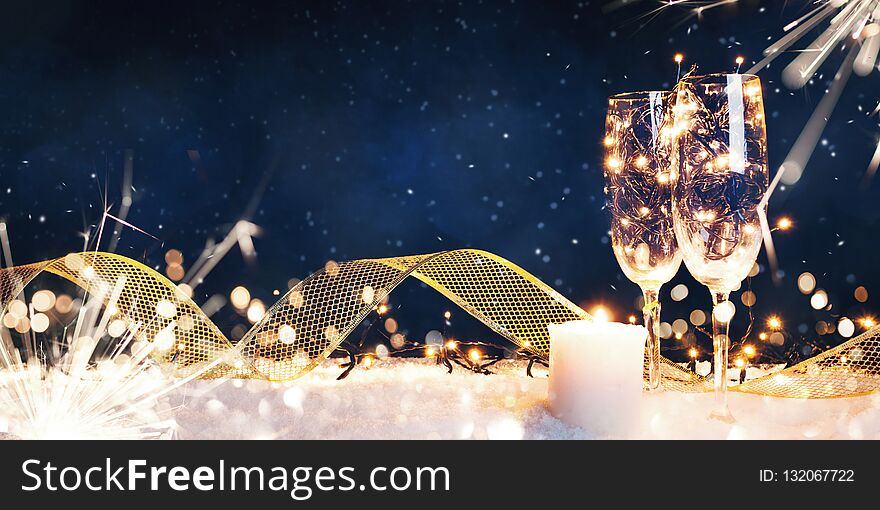 Two glasses filled with garlands with a candle and a gold ribbon in the snow. Christmas card