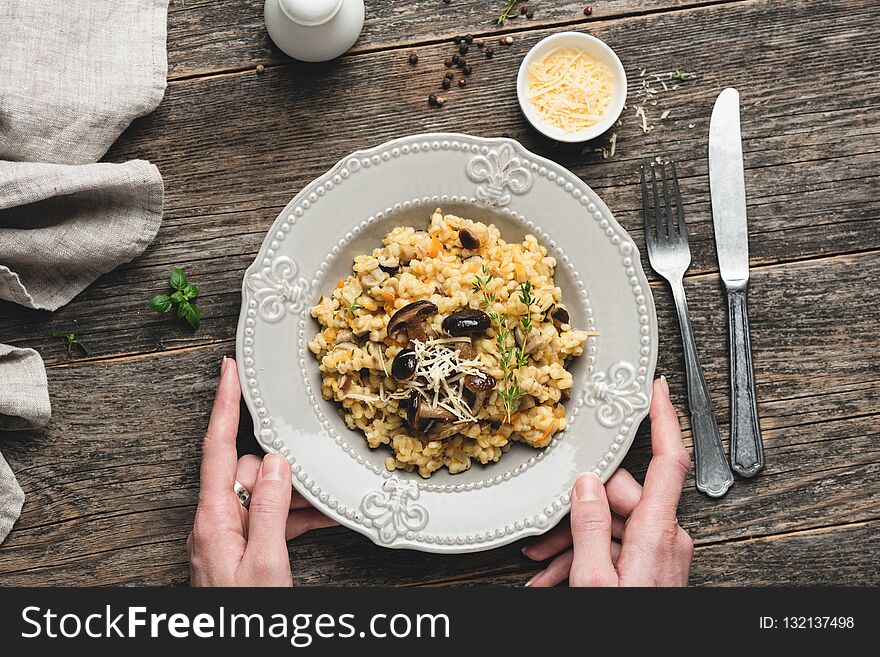 Barley mushrom risotto on plate over rustic wooden background with person holding a plate and vintage cutlery silverware table serving. Top view