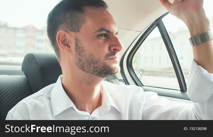 A young man with a beard rides in the back seat of the car.