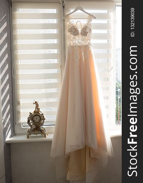 Bright beige wedding dress hanging on a hanger near a window. Bright beige wedding dress hanging on a hanger near a window