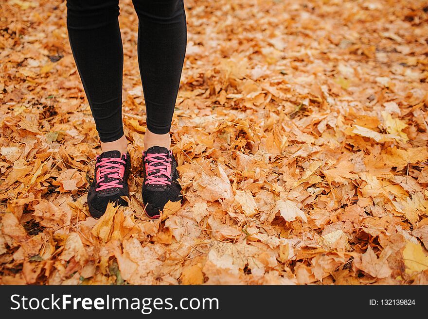 Cut view of young woman`s legs on autumn leaves. She has black with pink crosses and black pants. Woman is alone. She in park