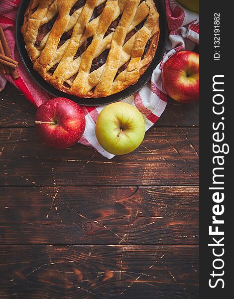 Homemade pastry apple pie with bakery products on dark rusty wooden kitchen table red and green apples and cinnamon. Traditional american dessert. Flat lay food background. Top view. Homemade pastry apple pie with bakery products on dark rusty wooden kitchen table red and green apples and cinnamon. Traditional american dessert. Flat lay food background. Top view