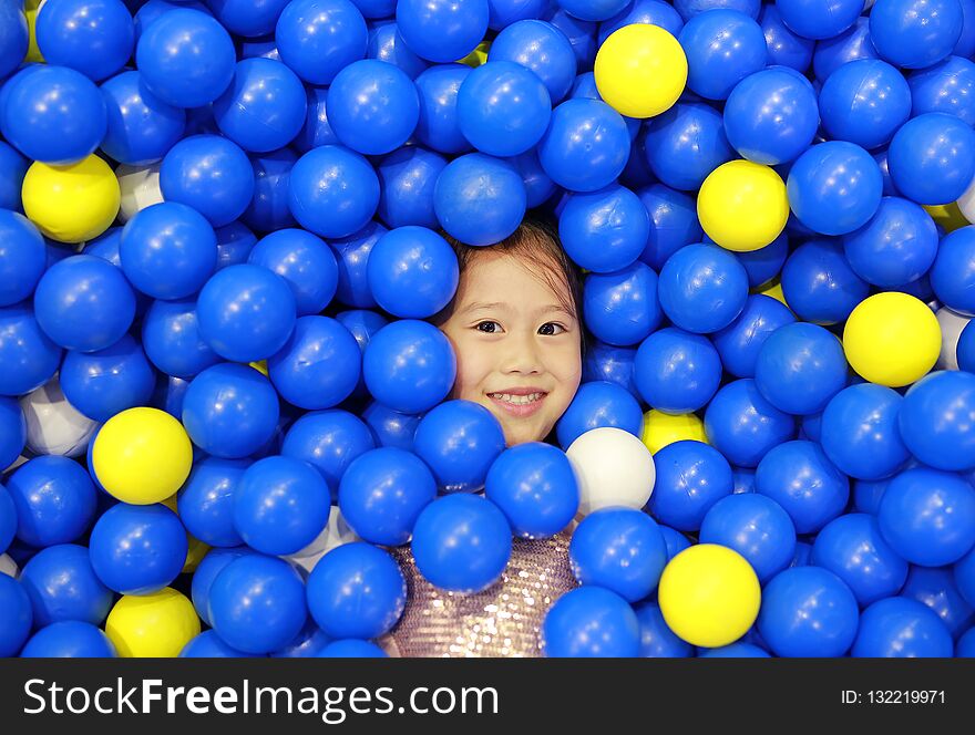 Smiling little girl playing with color plastic balls playground