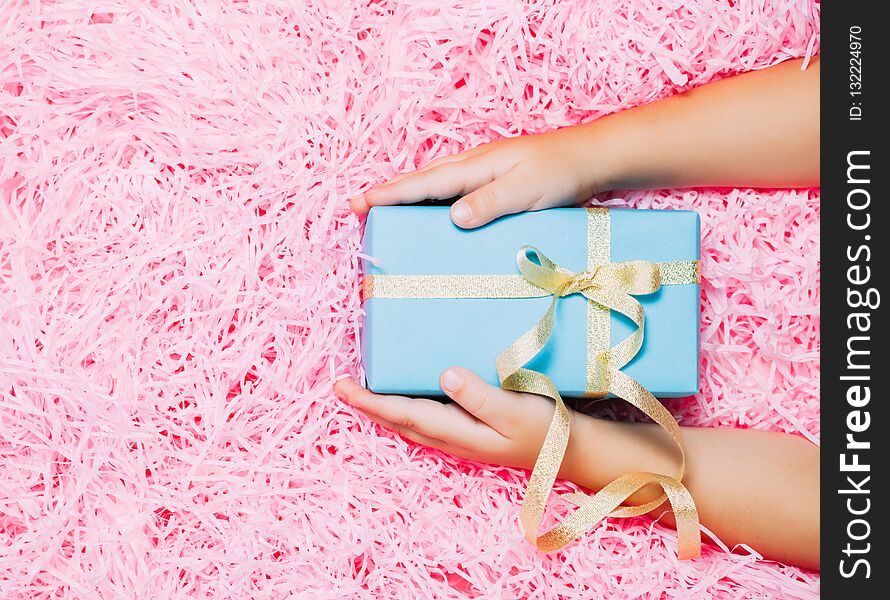 Child hands holding Christmas gift box on festive pink background. Top view, flat lay. Minimalism Christmas concept