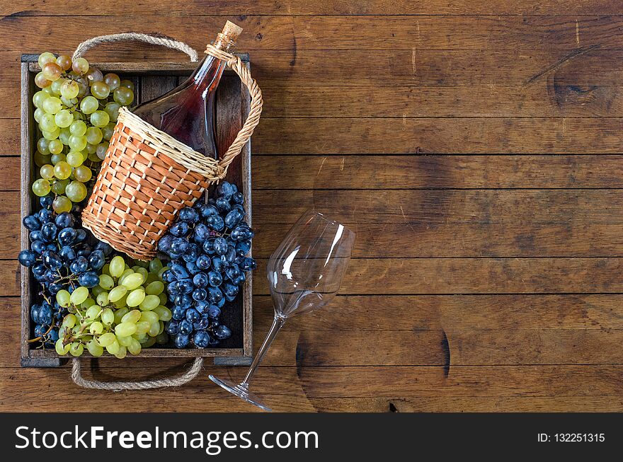Bottle with red wine, the bunches of ripe grapes in wooden box and a glass on wooden table. Top view, copy-space, rustic style. Bottle with red wine, the bunches of ripe grapes in wooden box and a glass on wooden table. Top view, copy-space, rustic style