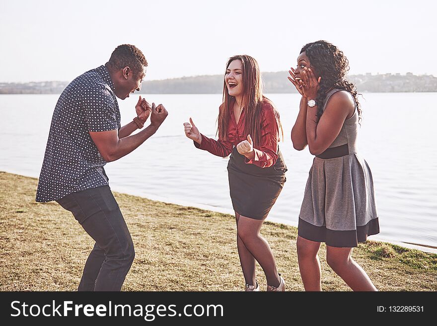 Group of friends having fun outdoors together. People relax and chat in the park on the shore of the lake.