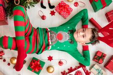 Cute Young Boy Wearing Xmas Pajamas Lying On The Floor, Surrounded By Christmas Presents, Ornaments And Decorations. Royalty Free Stock Photo