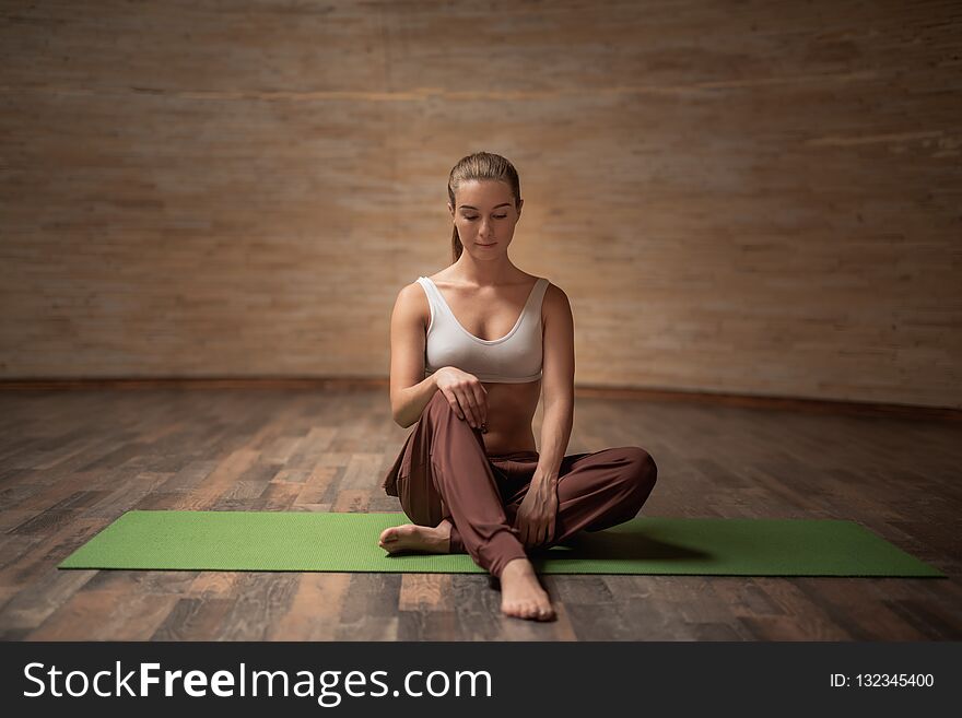 Peaceful young woman in comfortable clothes feeling relaxed while sitting on the yoga mat in empty room. Peaceful young woman in comfortable clothes feeling relaxed while sitting on the yoga mat in empty room