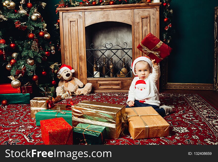Little Santa boy playing with gifts in decorated studio near fireplace.