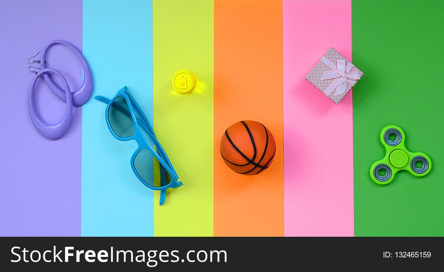 Trendy fashionable pastel composition with earrings, sunglasses, beverage can, basketball ball, gift box and spinner on background