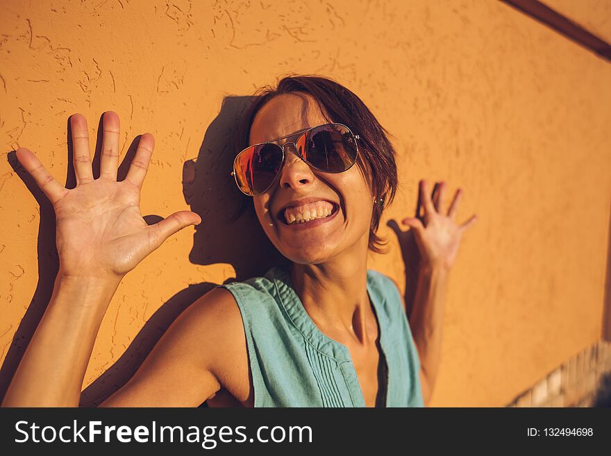 Portrait of a smiling woman. Girl on the background of an orange wall. A slender woman with glasses poses on a city street. A beautiful brunette is walking along a city street. Portrait of a smiling woman. Girl on the background of an orange wall. A slender woman with glasses poses on a city street. A beautiful brunette is walking along a city street