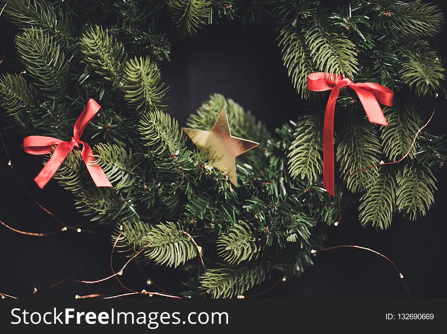 Blured dark New Year`s background fir-tree wreath with red ribbon tapes and a gold star